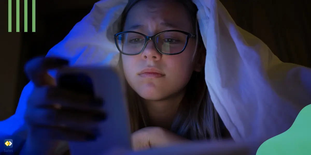 A girl looking at her phone screen under the blanket at night.
